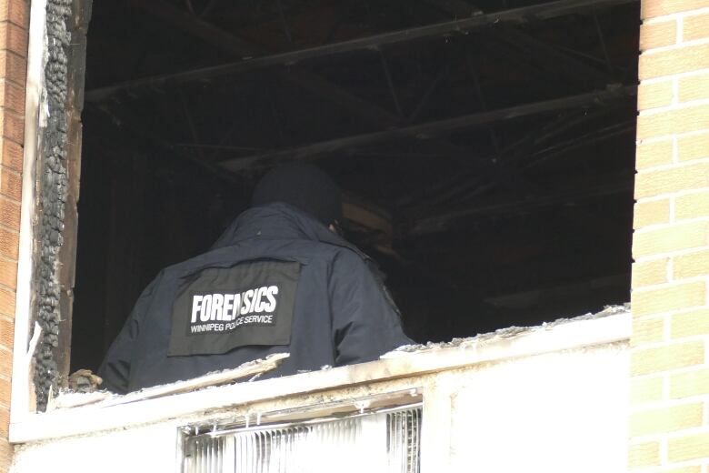 A police officer stands in front of a broken window.