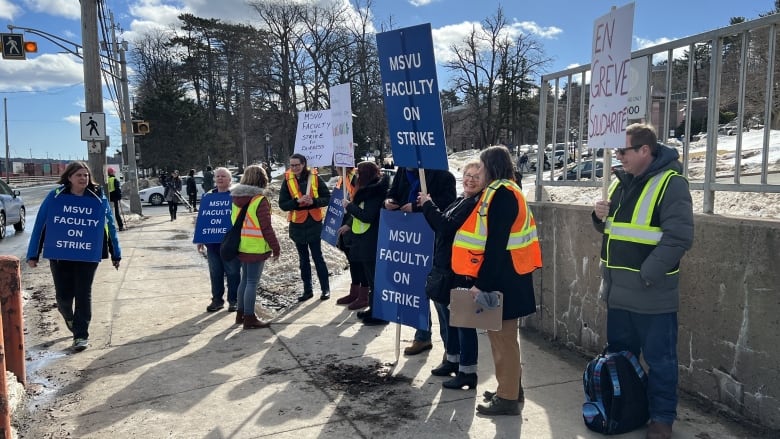 People stand on a sidewalk with signs.