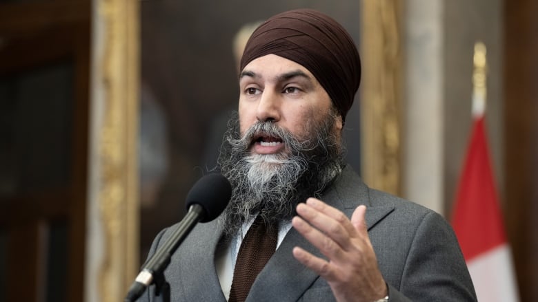 A man wearing a suit and a tie speaks at a microphone.