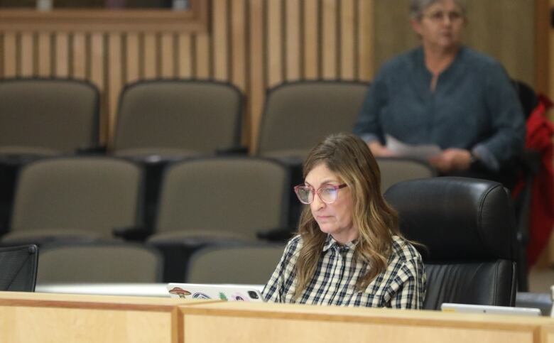 A woman in a black and white check shirt sits at a desk. 