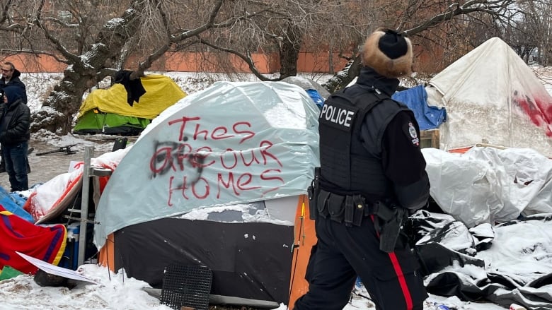 An Edmonton police officer passes in front of a tent that reads 