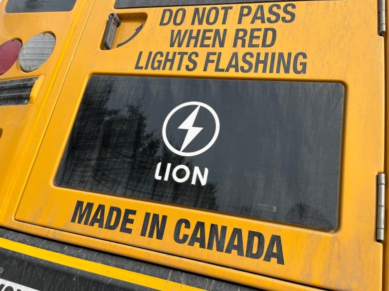 A Lion Electric logo is placed on a window on the back of a yellow school bus. 