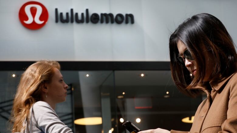 Two people passing a Lululemon store.