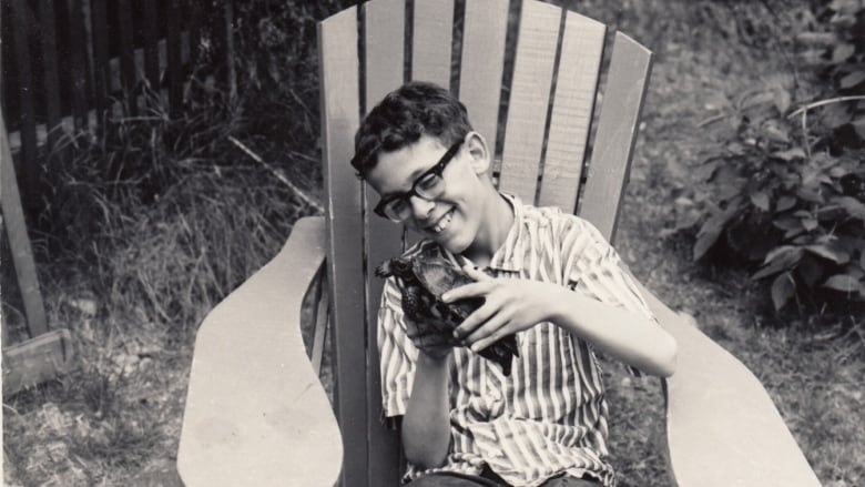 A black and white photo of a young boy with a big smile cuddling a turtle. 