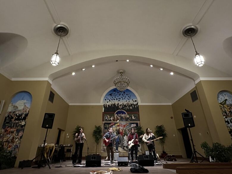 A band stands on a stage in a room with high ceilings. 