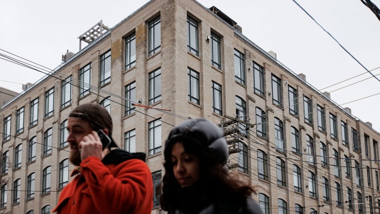 Two people wearing winter jackets walk by a large apartment complex.