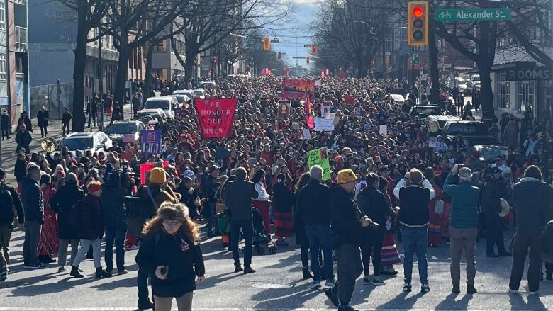 Hundreds of people, some carrying banners honouring missing and murdered Indigenous women (MMIW), walk down a street.