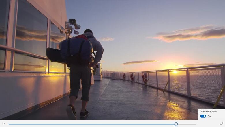 A man is pictured walking on a ferry deck with a sunrise in the background. 