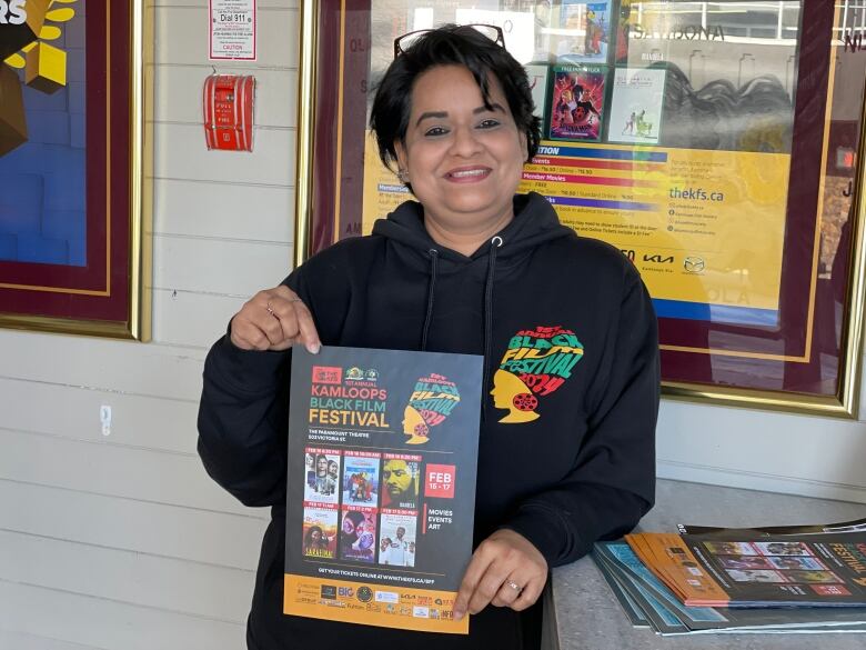 Smiling woman with dark skin and hair holds a poster for the film festival.