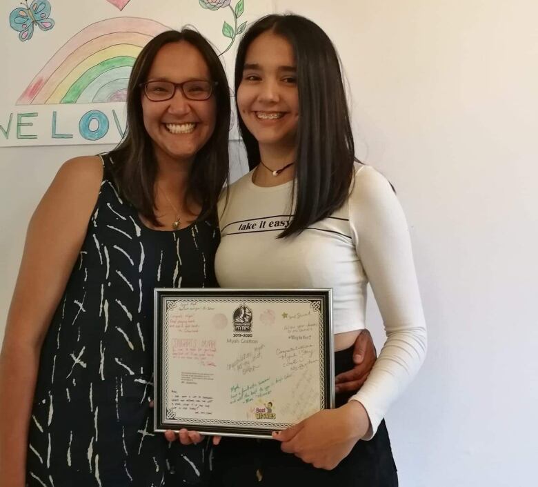 Teen girl and her mother stand together, smiling, while the girl holds a frame certificate.