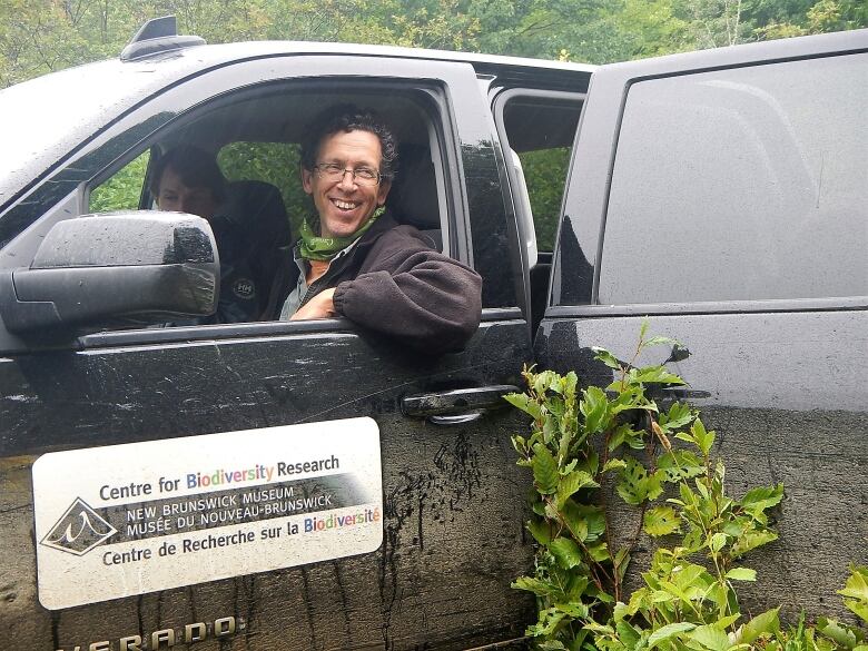 A smiling man in a pickup truck in the middle of the wilderness. 