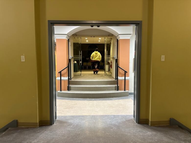 An open door shows steps leading into a room. A man wearing a yellow sweater stands in the doorway.