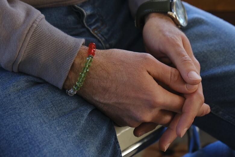 Ahmed has his hands folded together and is wearing a bracelet with red, green and white beads