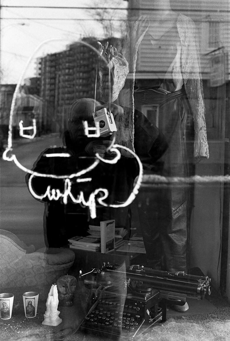 A black-and-white photo of a man's reflection in a store window.