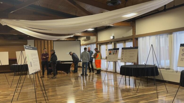 a group of people stand in a cluster in a room with presentation boards 