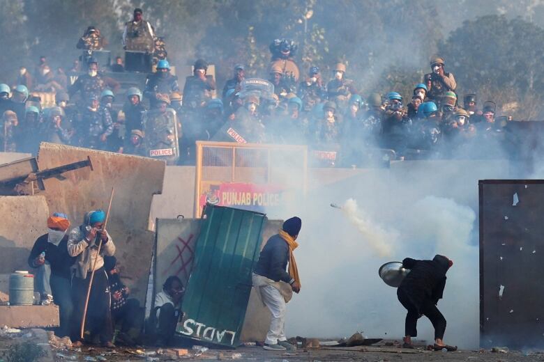 Farmers standing in the foreground throw tear gas back at police in the background. 