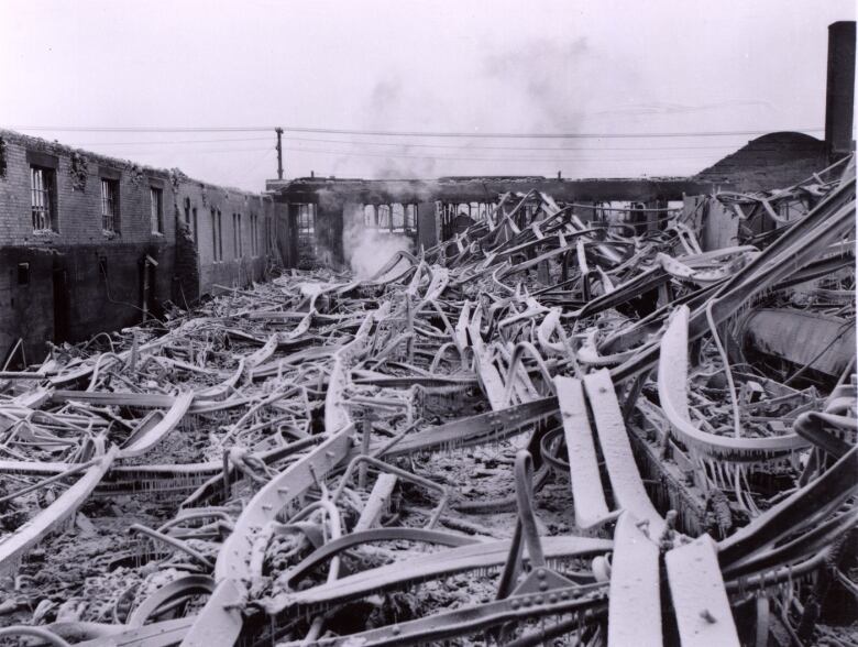 Smoke rises from a pile of twisted metal and rubble The husk of a burnt-out streetcar sits in the background.