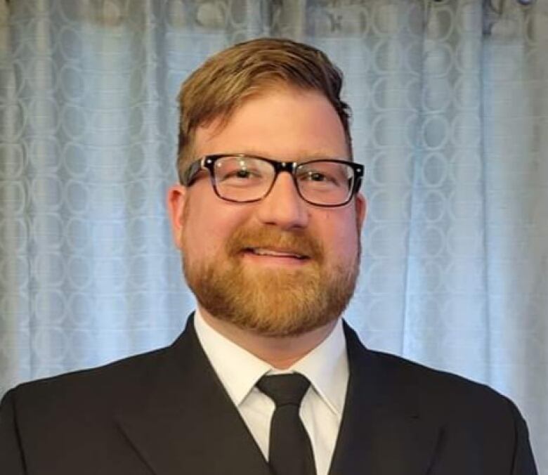 A red-headed man with a beard and glasses smiles at the camera.