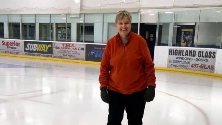 Smiling woman wearing a red sweater skates in a rink.