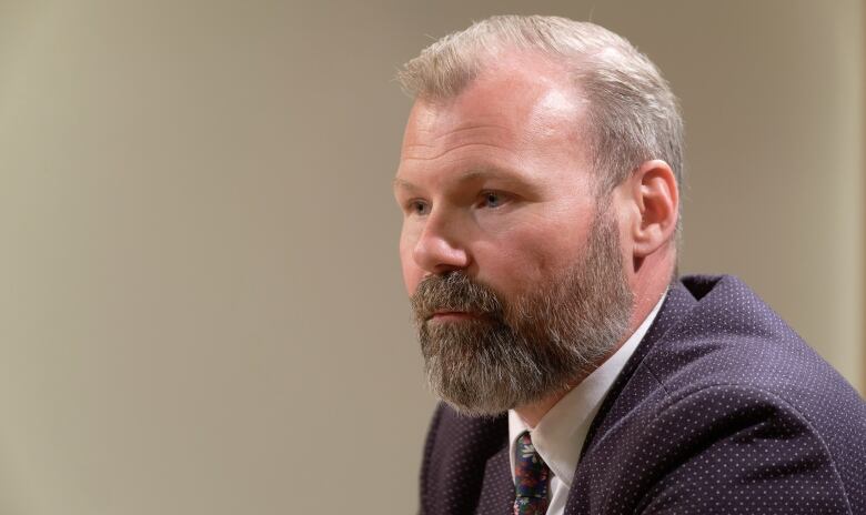 A man with a beard is pictured. He is also wearing a suit.