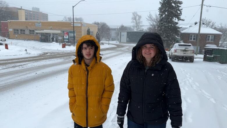 A teenage boy in a yellow coat and a woman wearing a black coat, walking out in the snow.