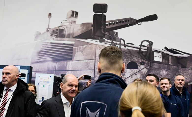 People stand in front of a mural of a tank.