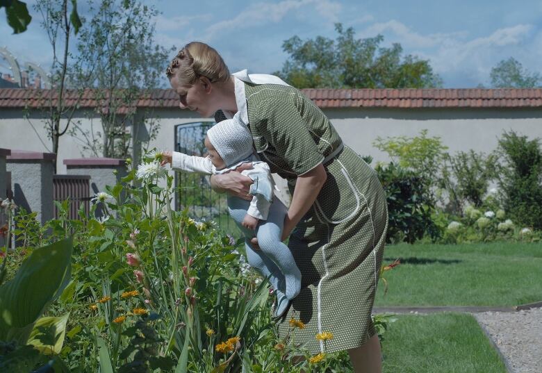 An adult holds up a baby as they interact with flowers.