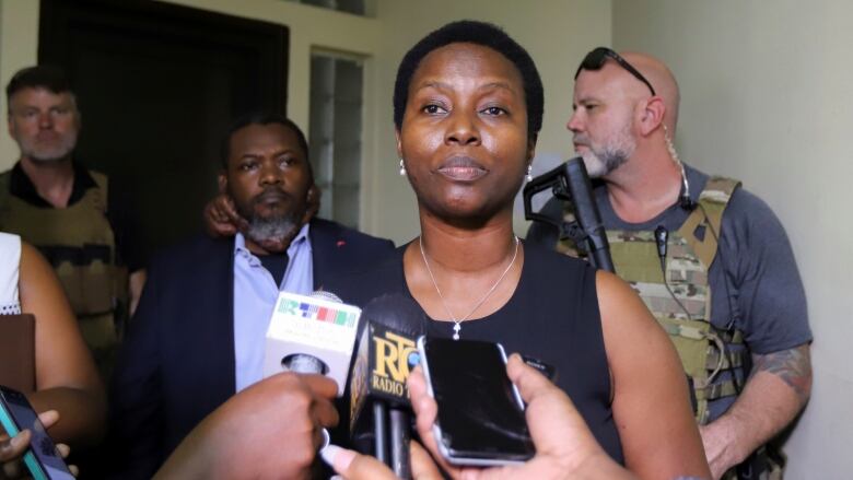 A woman wearing a sleeveless top stands before microphones.