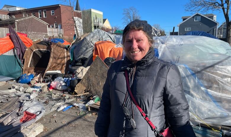 A smiling woman stands bundled up in front of a row of colourful tents. 