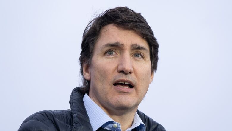 A man in a rain jack and blue collared shirt speaks.