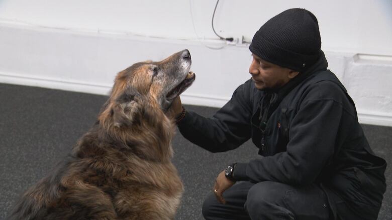 A man crouches and pets a dog.