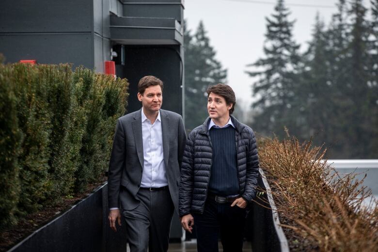 Two tall white men walk next to rows of shrubbery.