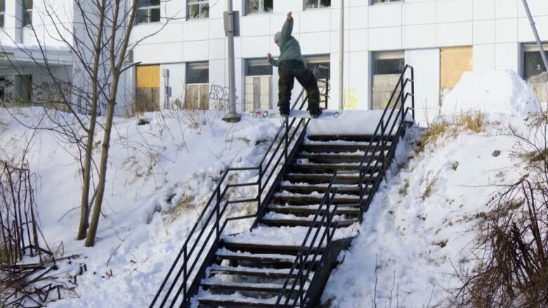 Man on snowboard slides down the railing next to a set of stairs. 