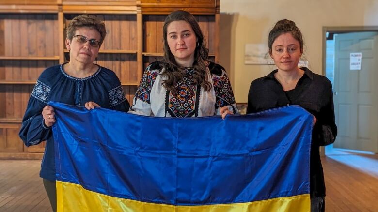 Three women hold a Ukrainian flag 