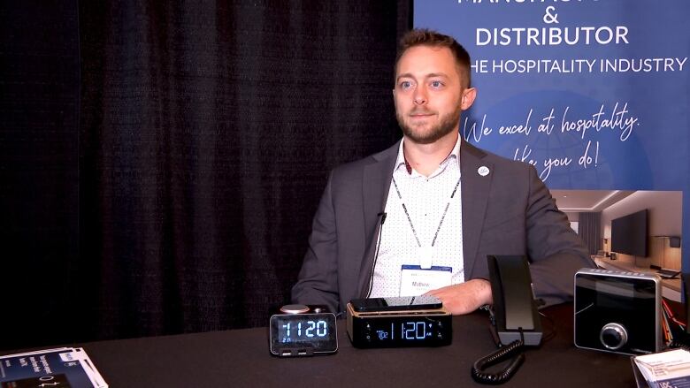 Man in a suit in front of a blue poster, with clocks in front of him. 