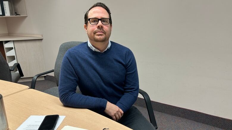 A man with a beard and glasses sits at a table 