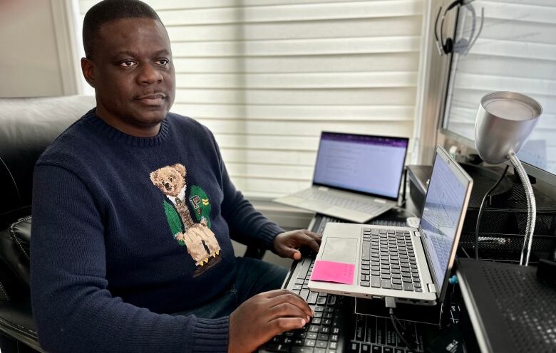 A man sits at a desk that is crowded with several laptops and computer keyboards. 