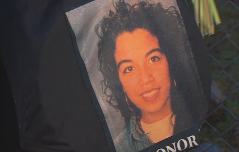 A woman holds up a picture of an Indigenous woman, who is smiling.