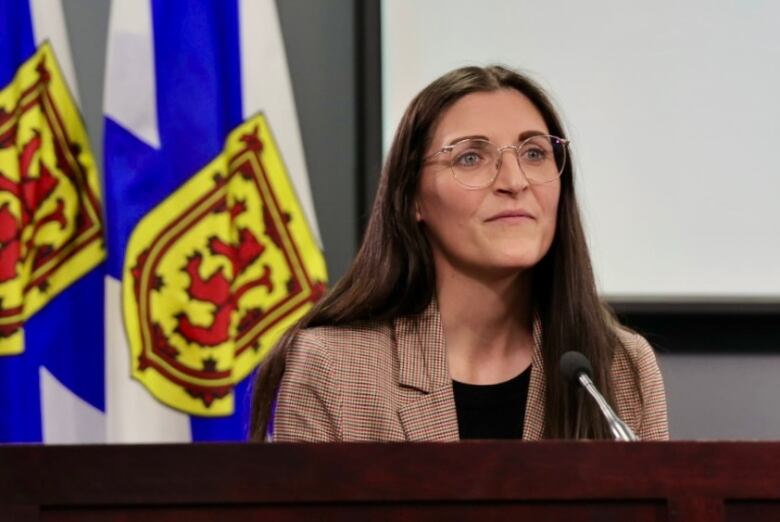 A woman sits in front of Nova Scotia flags.