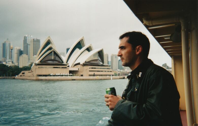 A man with black hair is shown with the Sydney Opera House behind him.