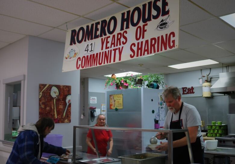 Two soup kitchen volunteers serve food to a man in a blue plais jacket. 