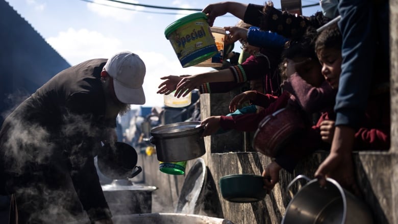 A number of people hold out pots for food.