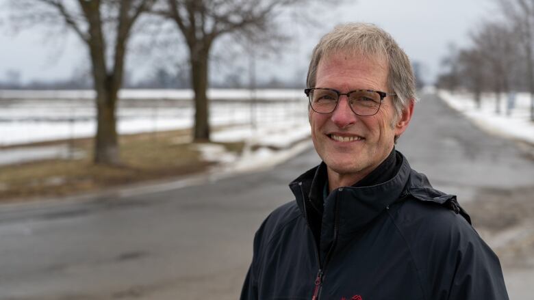 A man stands in front of a farm field in winter.