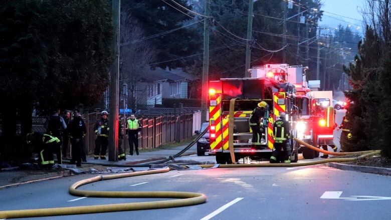 A firetruck is pictured on a street, its hose snaking toward the left of the images while a few people in what appears to be police and firefighting gear are seen off the side. 