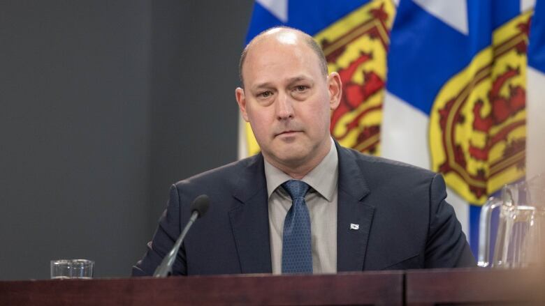 A bald man sits in front of flags.