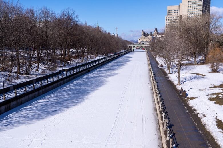 A snowy canal on a sunny late-winter day. Snow has partially melted on the grassy areas beside it.