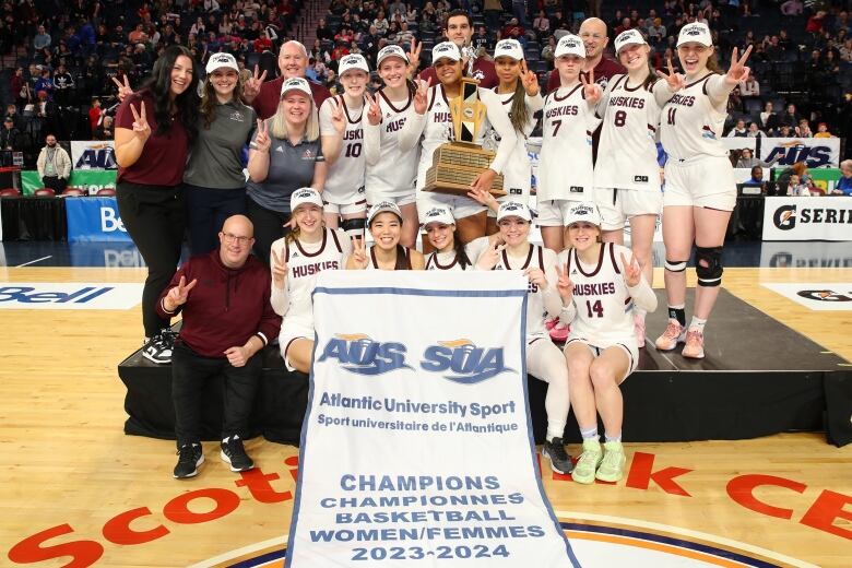 A women's basketball team, wearing their uniforms, poses with their banner.