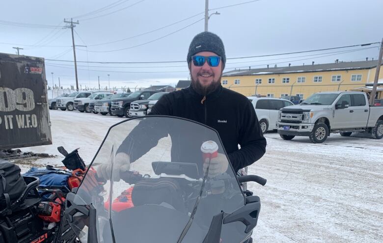 A man smiles while sitting on a snowmobile.