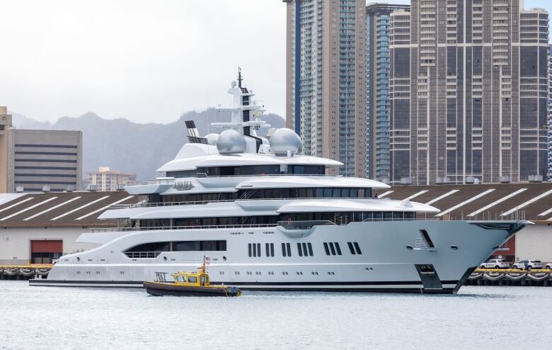 A large, white yacht docked in front of tall buildings. 