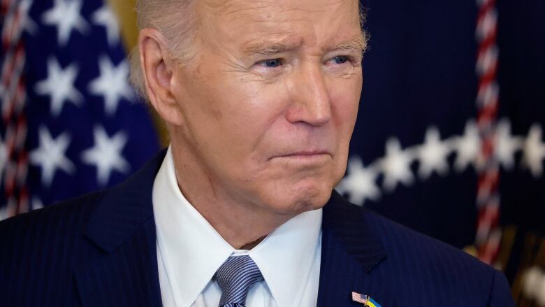 Close-up of President Joe Biden looking to one side, an American flag visible behind him.